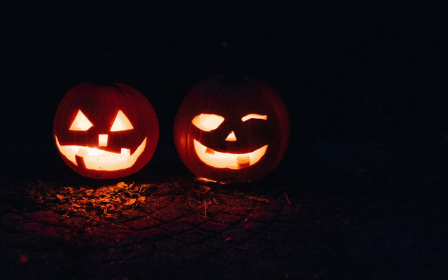 Two glowing jack-o'-lanterns on the ground at night (photo: Beth Teutschmann, Unsplash)